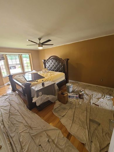 Bedroom being painted; bed covered in sheets; one wall is brown, other walls cream-colored.
