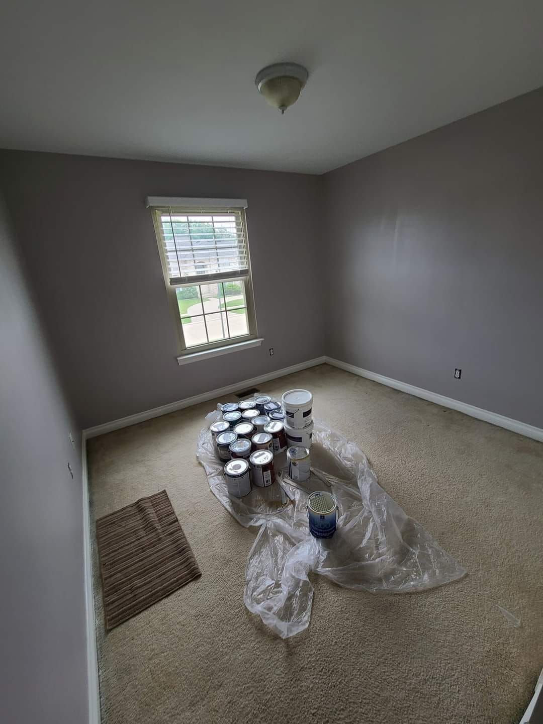 Room with gray walls, a window, and paint cans on the floor, likely for painting.