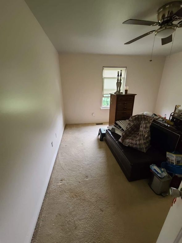 Room with dirty carpet, brown dresser, and a ceiling fan.