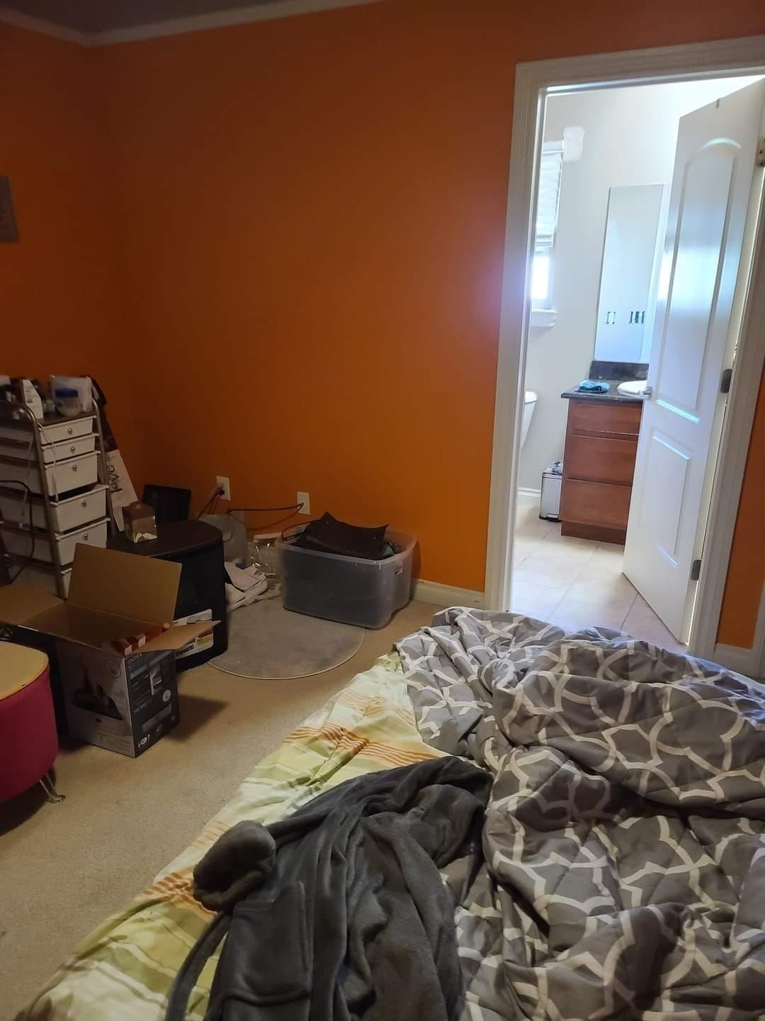 Orange bedroom with unmade bed, open doorway to bathroom, clutter on floor.