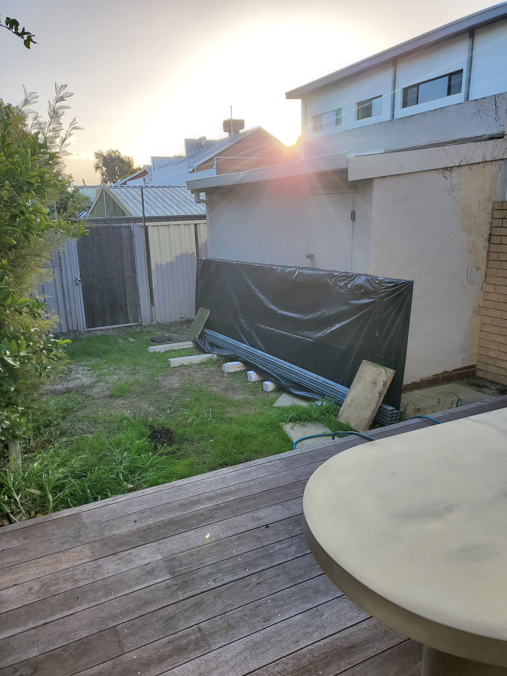 Backyard scene; wooden deck, grassy area, shed with black tarp, sun shining.