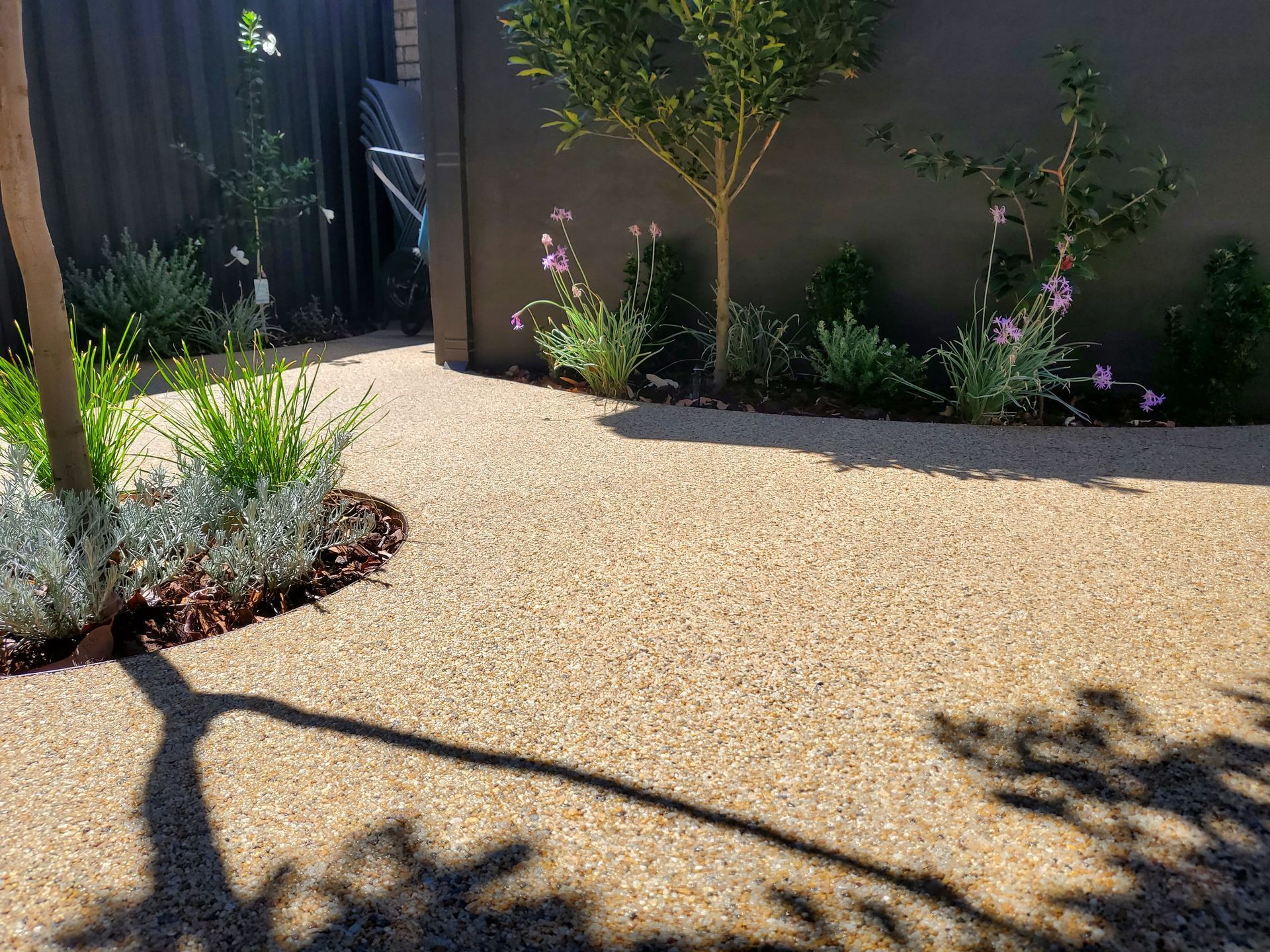 StoneSet Resin Permeable Surface in Cudgee Beach tones with lush plants and small trees against a dark gray wall.