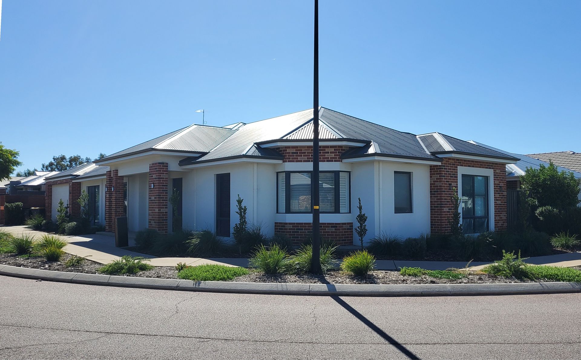 A modern house with a gray roof and brick accents on a sunny day with a tree and blue sky with puffy clouds.