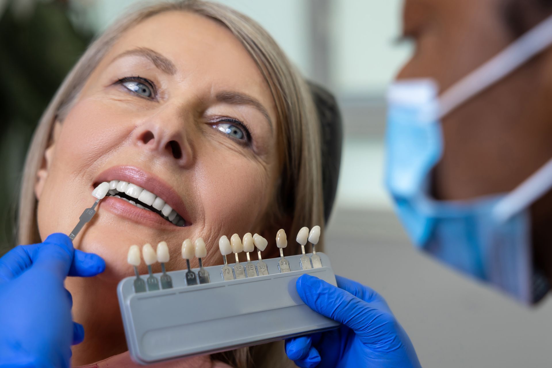 Patient in dentist's seat while doctor choosing the shade of dental veneer according to color chart Patient in dentist's seat while doctor choosing the shade of dental veneer according to color chart