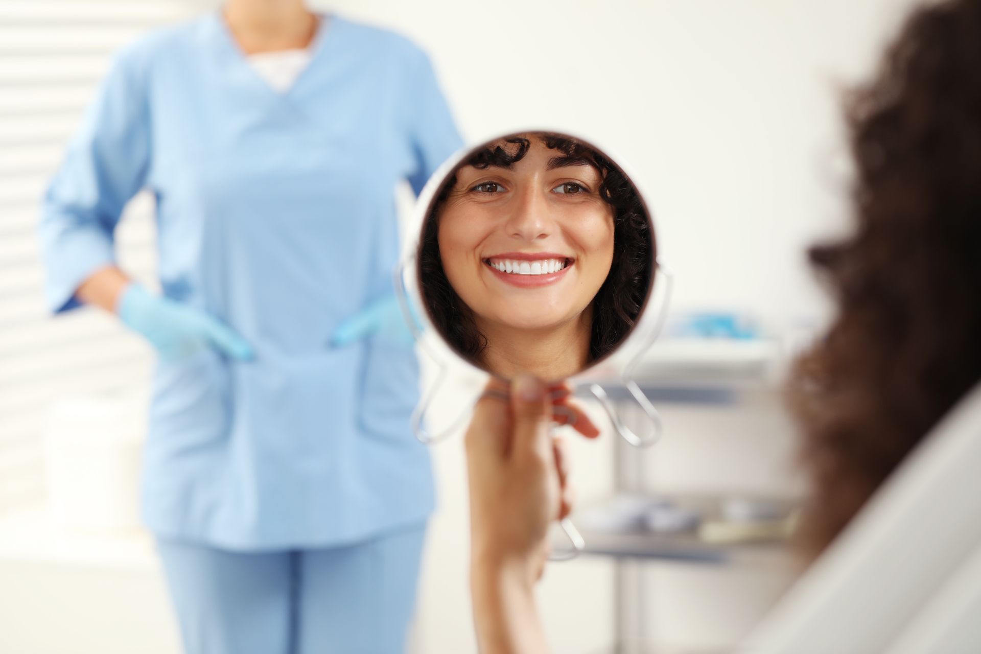 Patient looking in a mirror and a dentist in the background after inserting dental veneers.