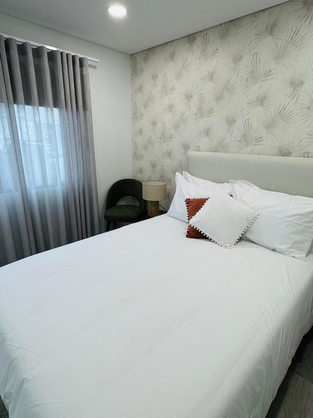 A bedroom with a queen bed featuring white linens and decorative pillows, gray curtains, and a patterned accent wall.
