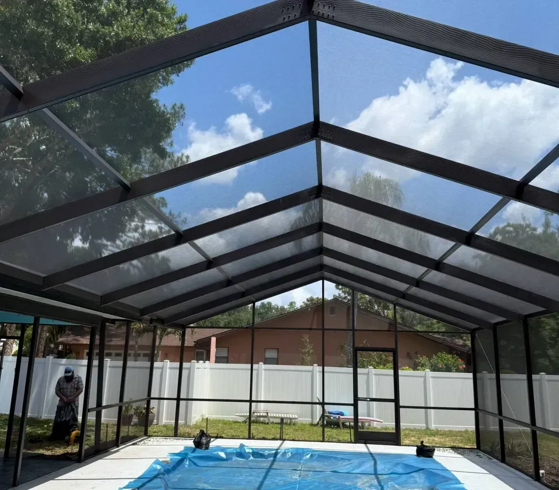 A blue pool cover lies in an outdoor swimming pool enclosed by a metal frame and insect screening under a sunny sky.
