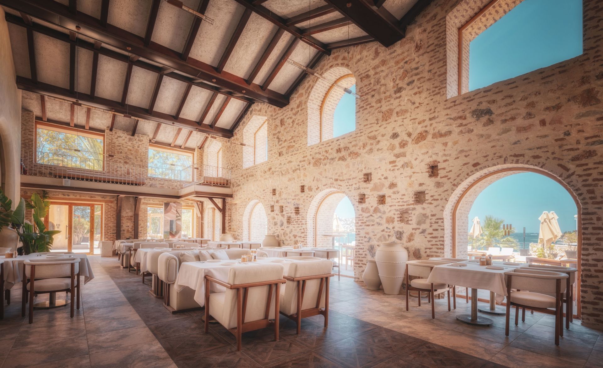An elegant, rustic restaurant interior with stone walls, arched windows, and white-clothed tables under a beamed ceiling.