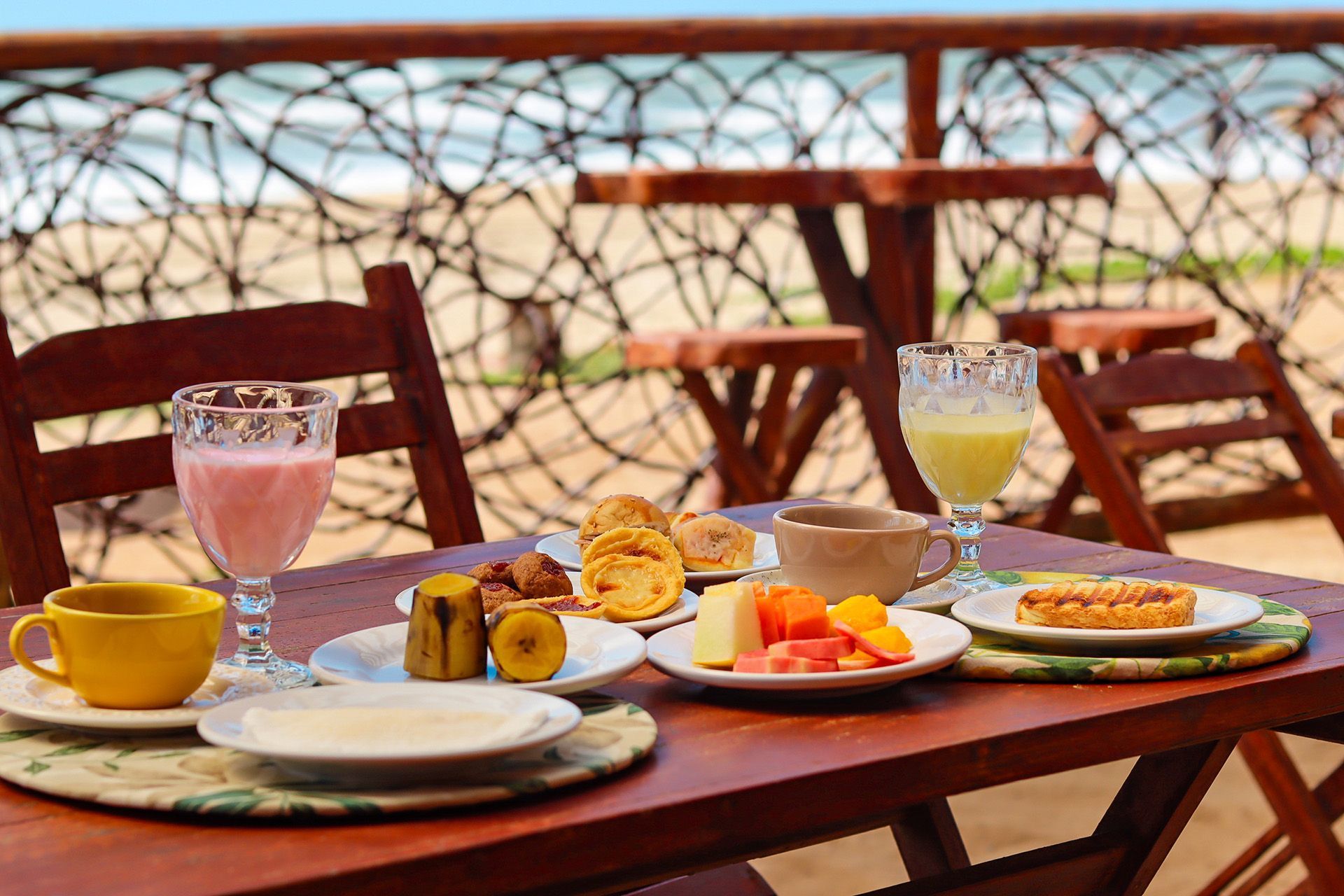Mesa de café da manhã posta com comidas e bebidas com vista para a praia.