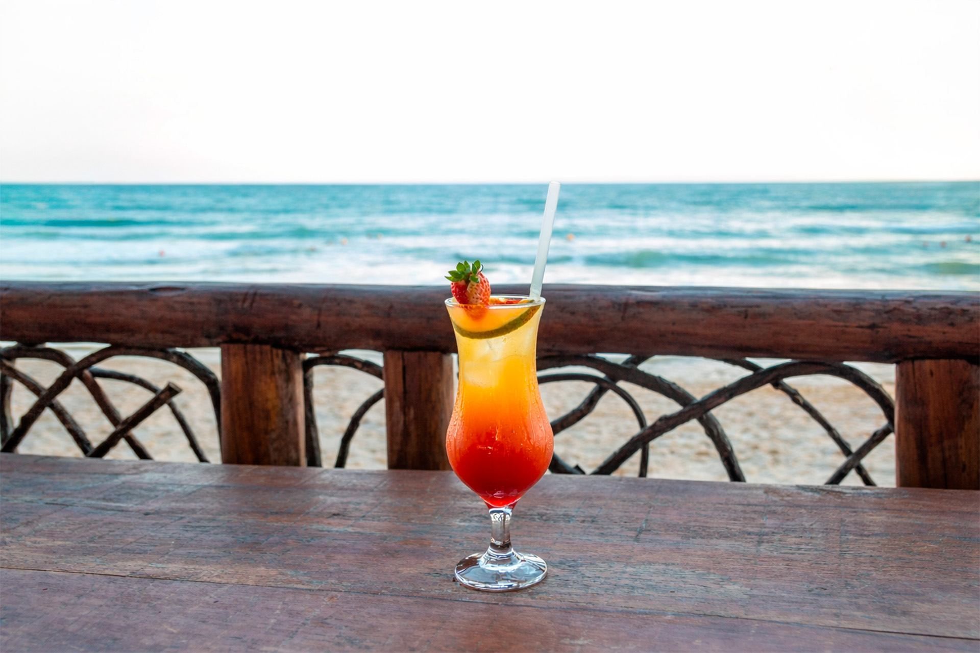 Coquetel sobre uma mesa de madeira com vista para a praia ao fundo.