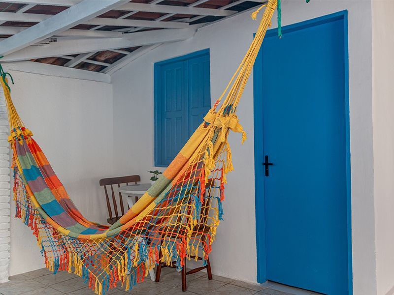 Rede colorida pendurada em um prédio branco com porta e janela azuis.