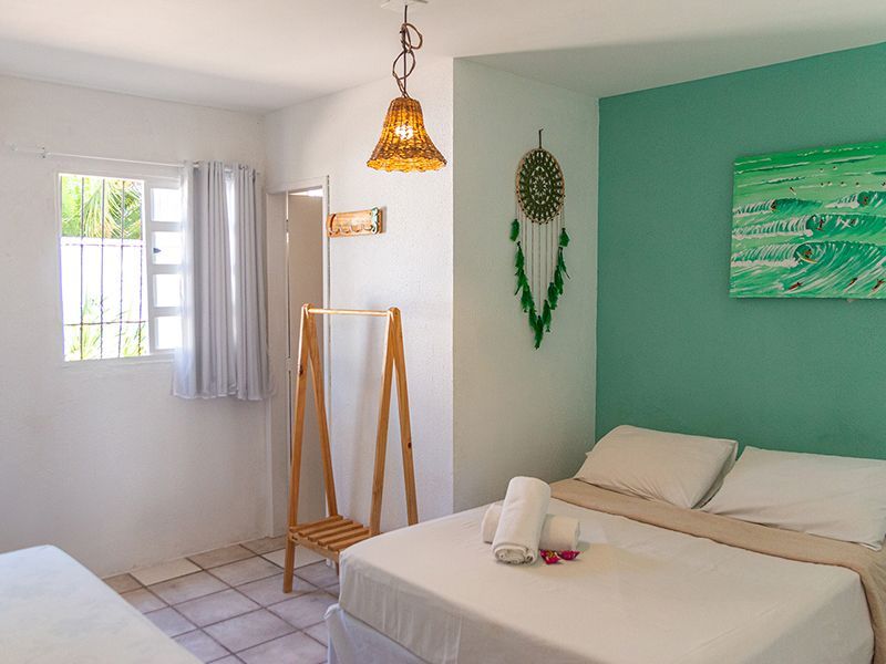 Quarto com paredes brancas, duas camas e uma parede com detalhes em turquesa, incluindo uma obra de arte e um apanhador de sonhos.