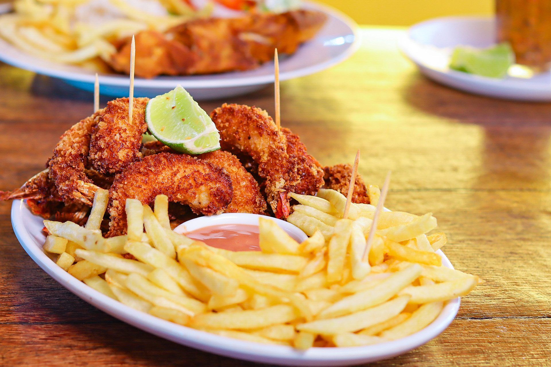 Prato de tiras de frango frito com batatas fritas, molho para mergulhar e uma fatia de limão.