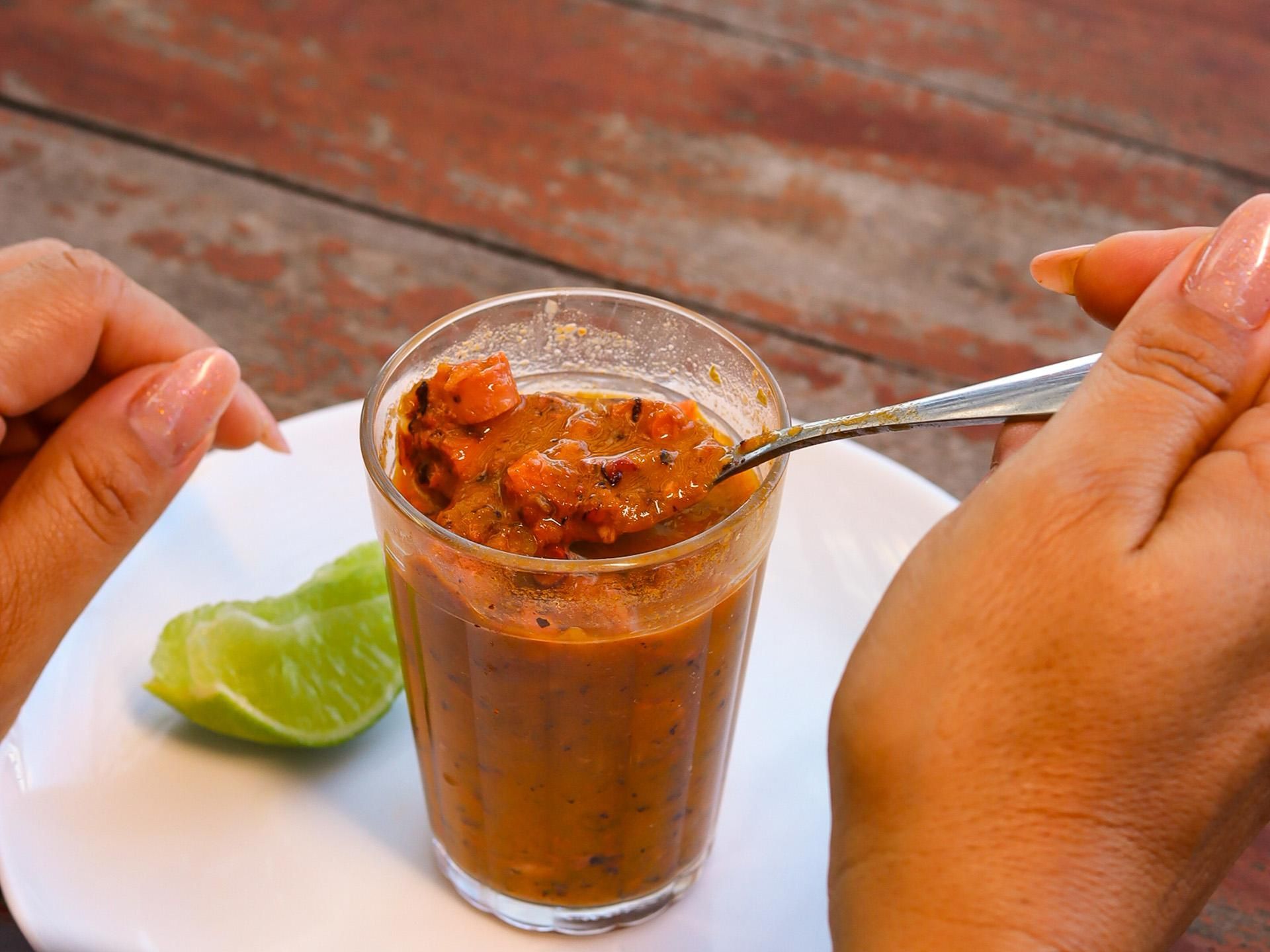 Pessoa comendo um molho espesso e marrom de um copo com uma colher; fatia de limão ao lado.