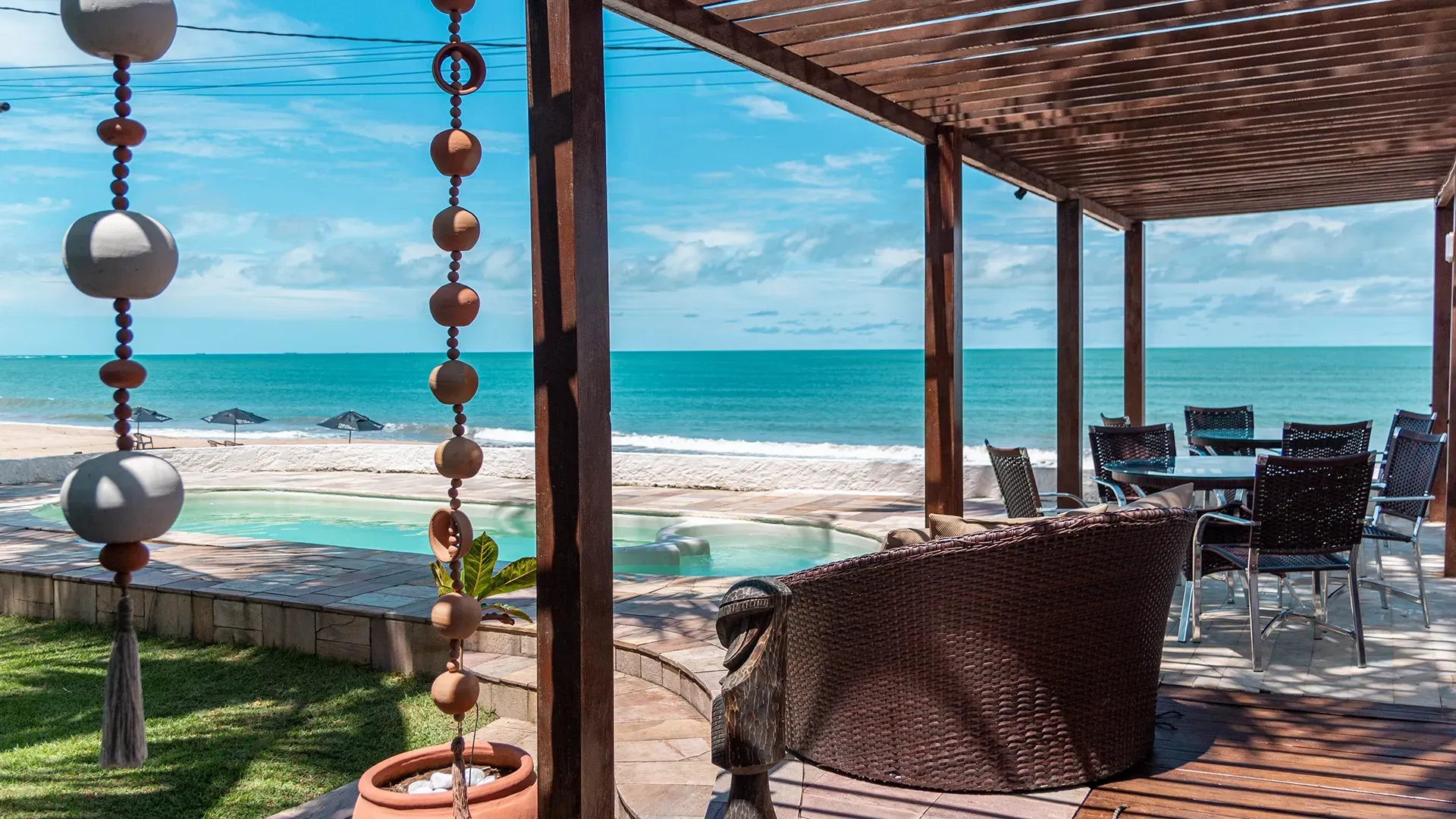 Pátio à beira-mar com vista para o oceano, móveis de vime e ornamentos decorativos pendurados.