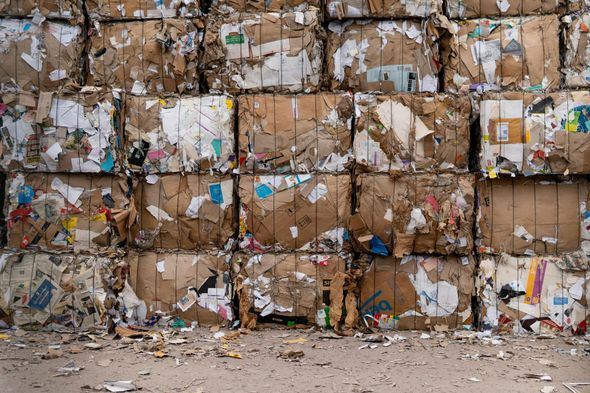 Stacked bales of compressed cardboard, ready for recycling; brown and white with scattered color.