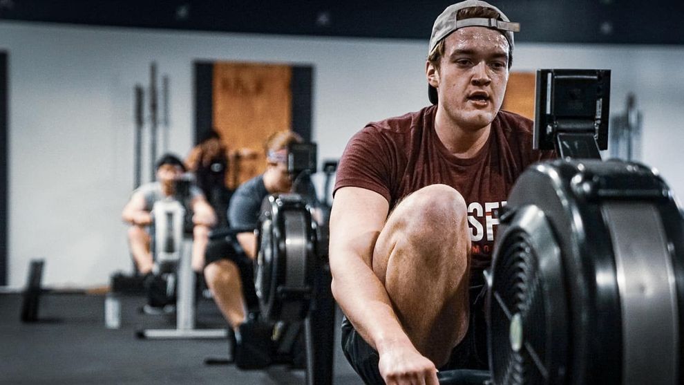 A man is riding a rowing machine in a gym.