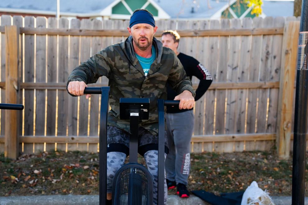 A man is riding an exercise bike in front of a wooden fence.