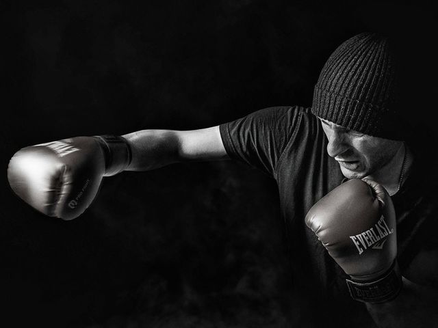 A black and white photo of a man wearing boxing gloves and a beanie.