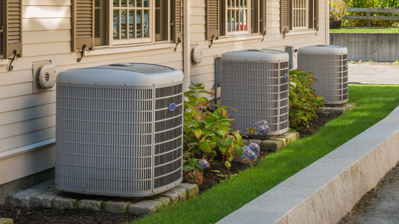 A row of air conditioners are sitting outside of a house.