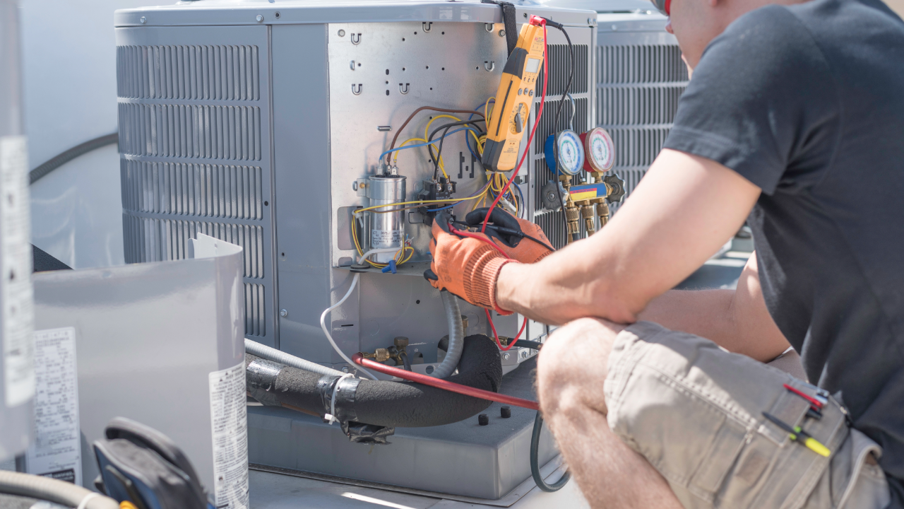 A man is kneeling down working on an air conditioner.