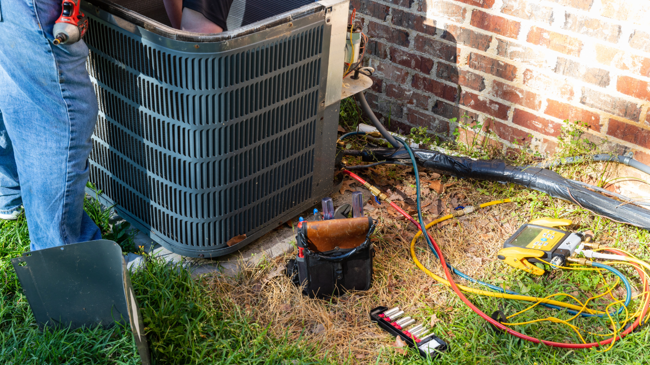 A man is working on an air conditioner outside of a house.