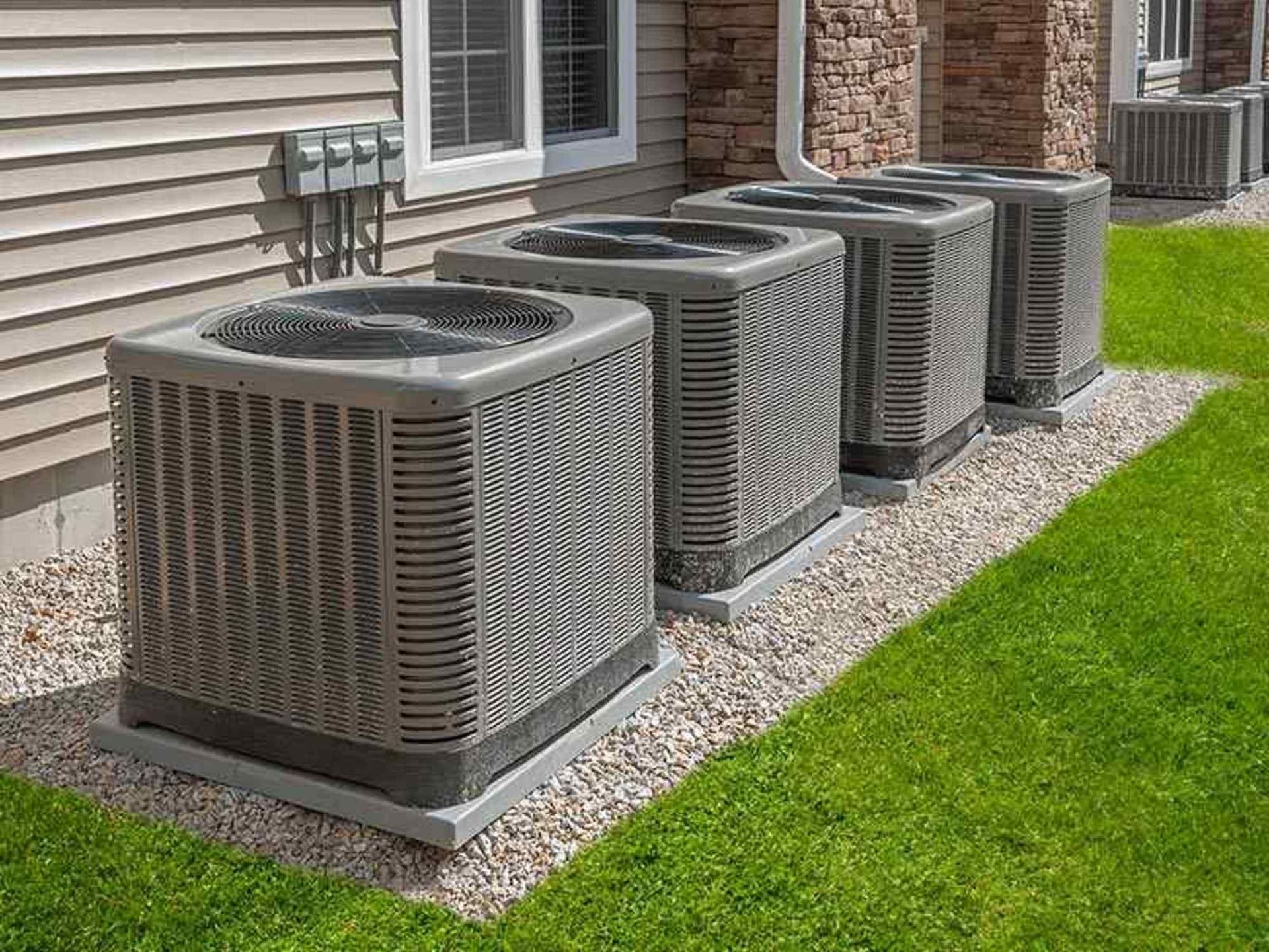 A row of air conditioners are sitting in front of a house.