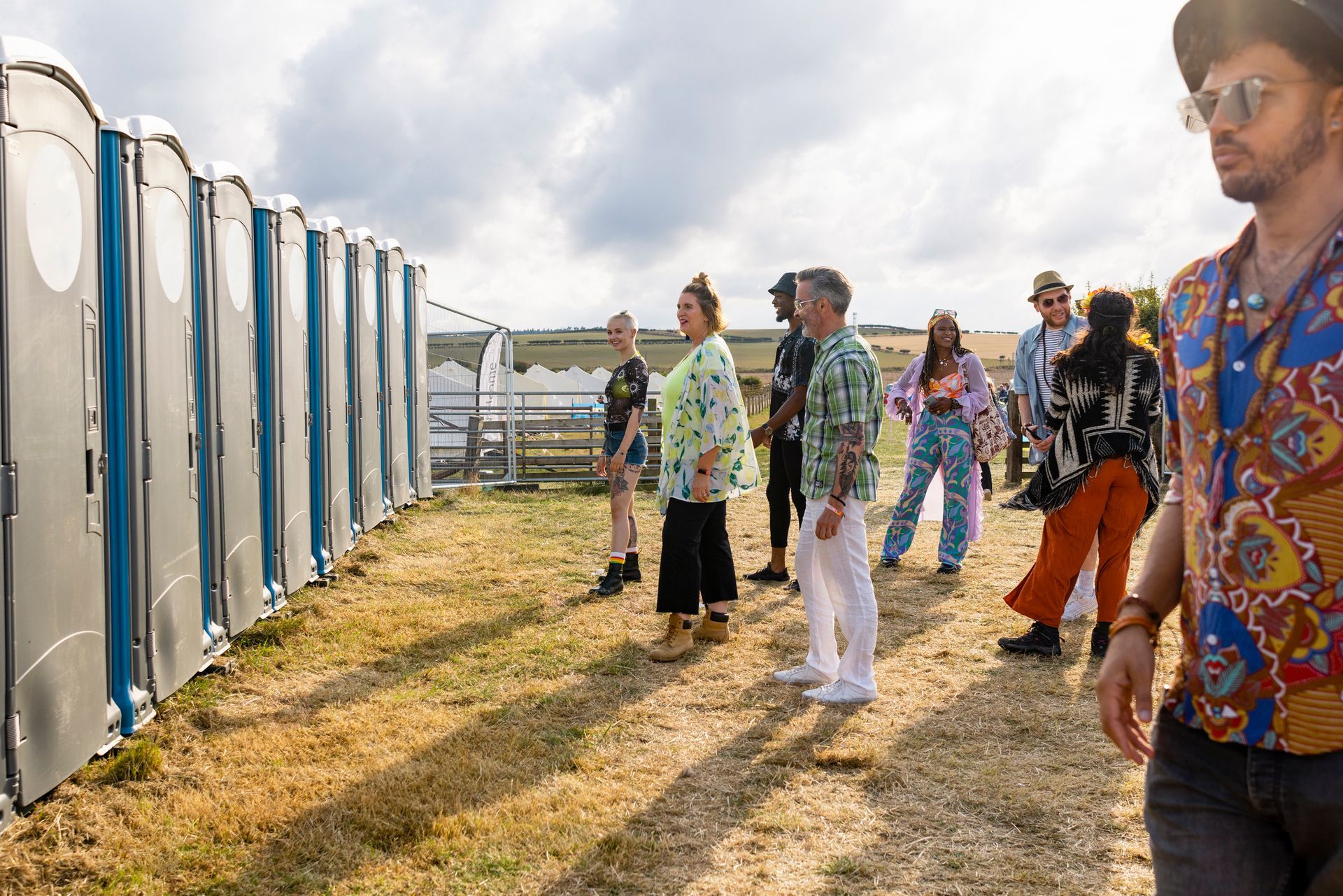 A group of people queuing in line for the portable toilet at an event.