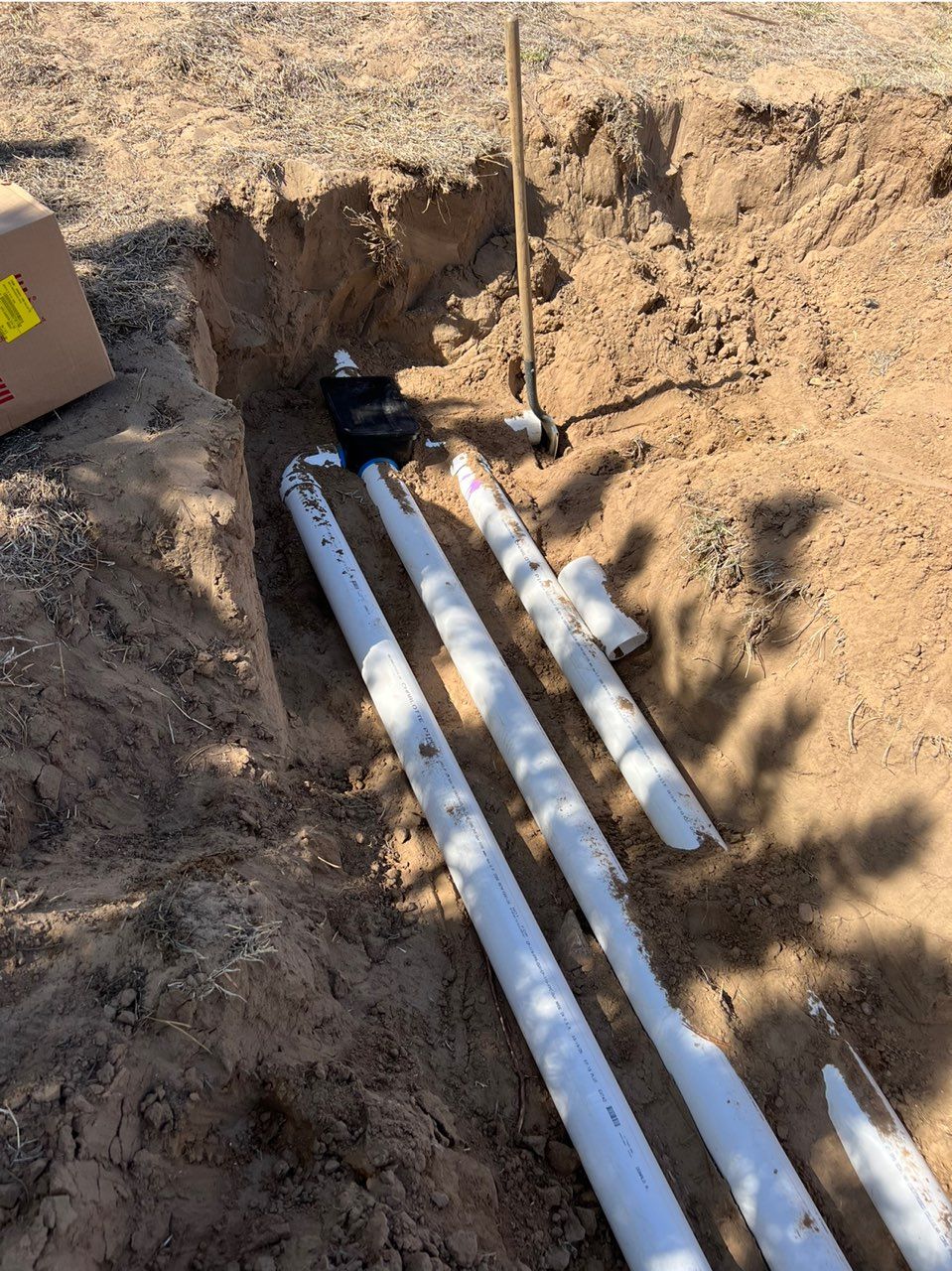 Pipes in a trench, near a shovel and soil, outdoors.