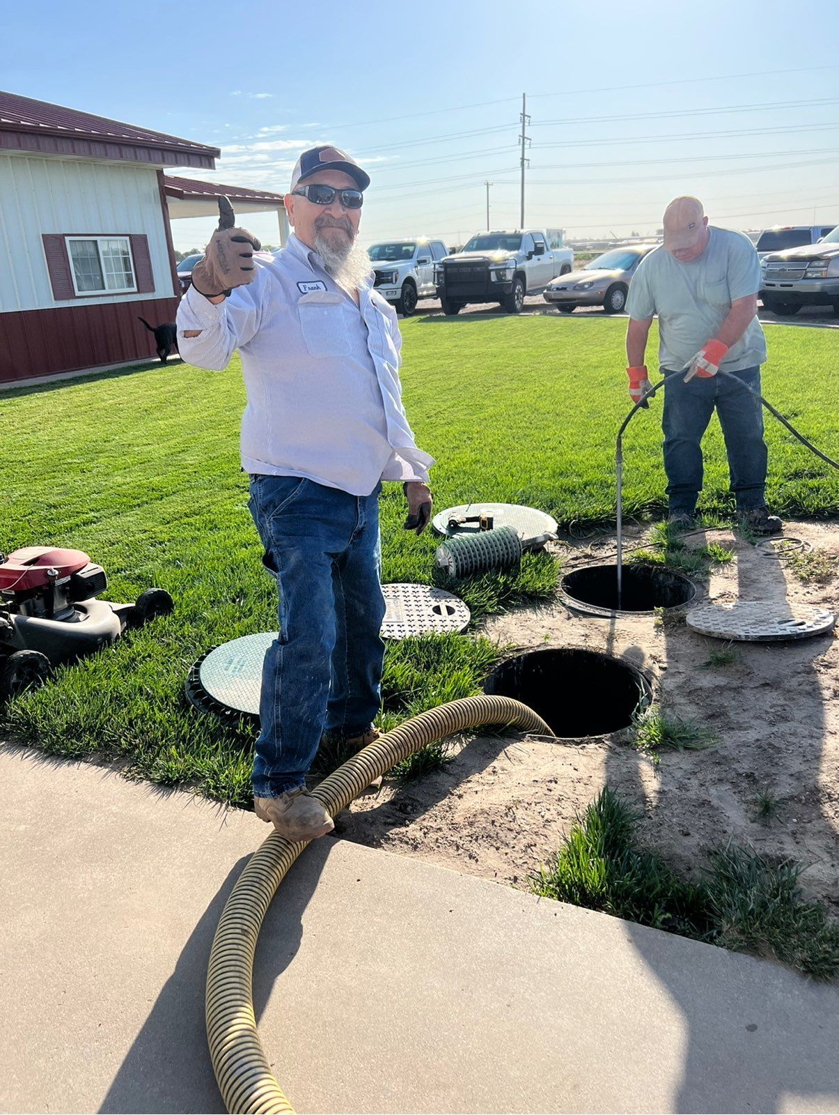 Two men working on septic tanks outdoors, one giving a thumbs up.