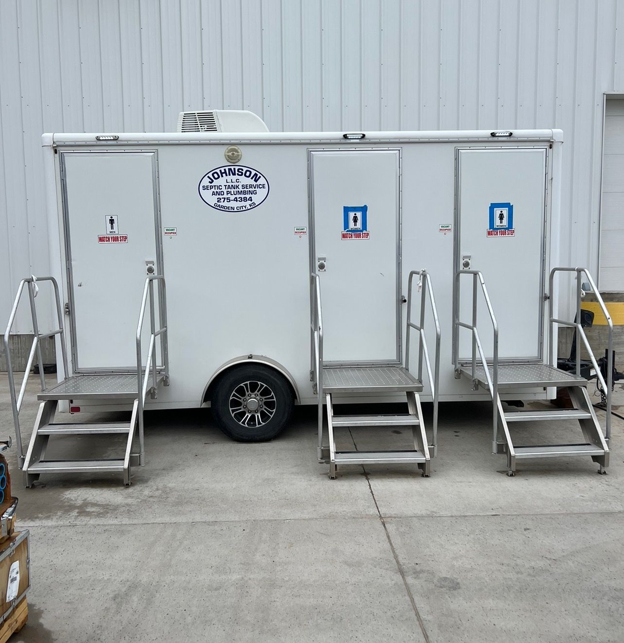 White portable restroom trailer with three stalls, each with steps.