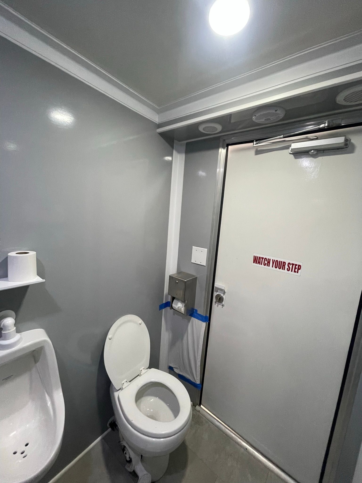 Gray public restroom with a toilet, urinal, and closed door.