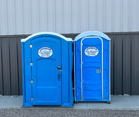 Two blue portable toilets are sitting in a grassy field.