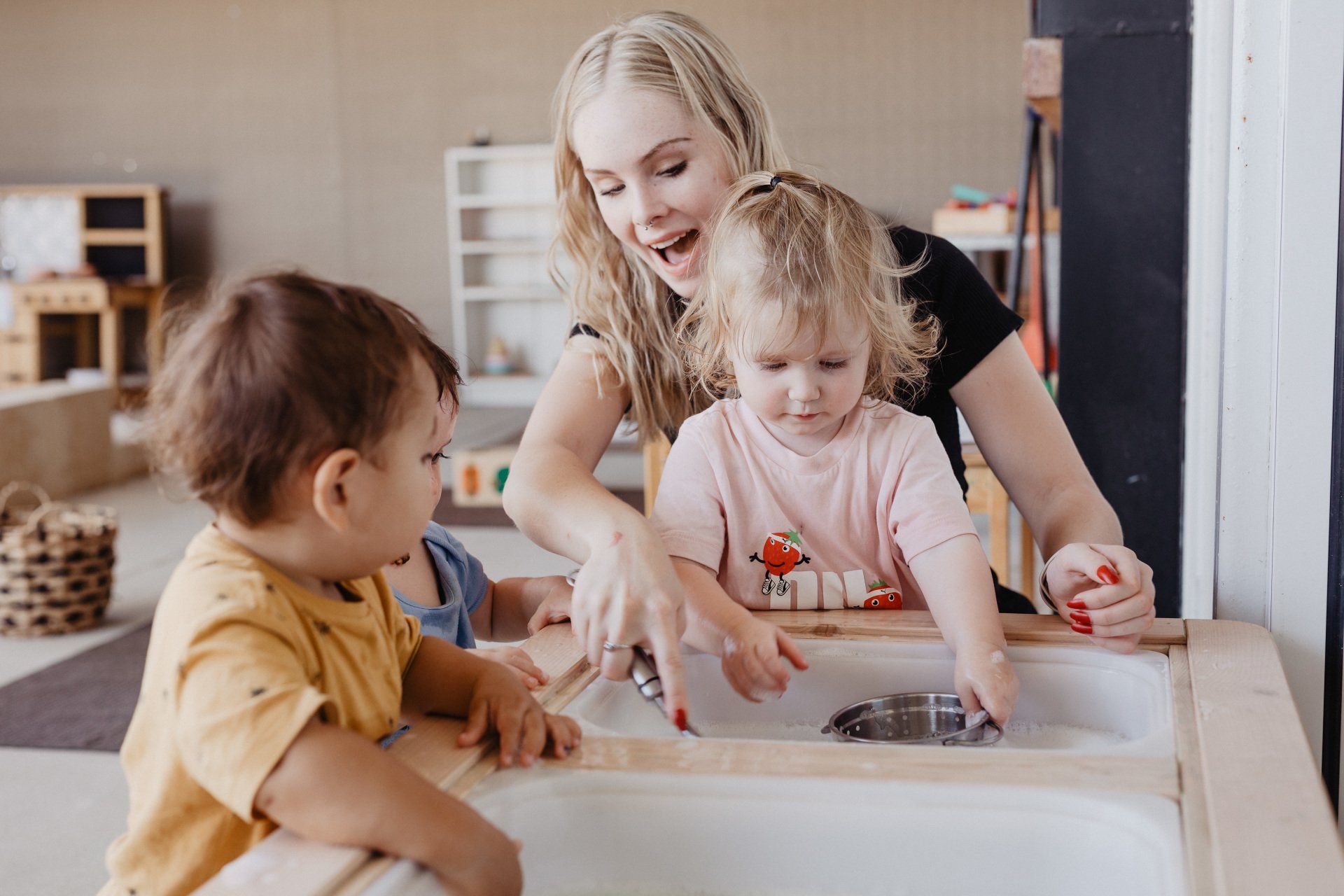 A woman and two children are having fun playing in a sink at the Sagewood Joondalup Campus Childcare Centre.