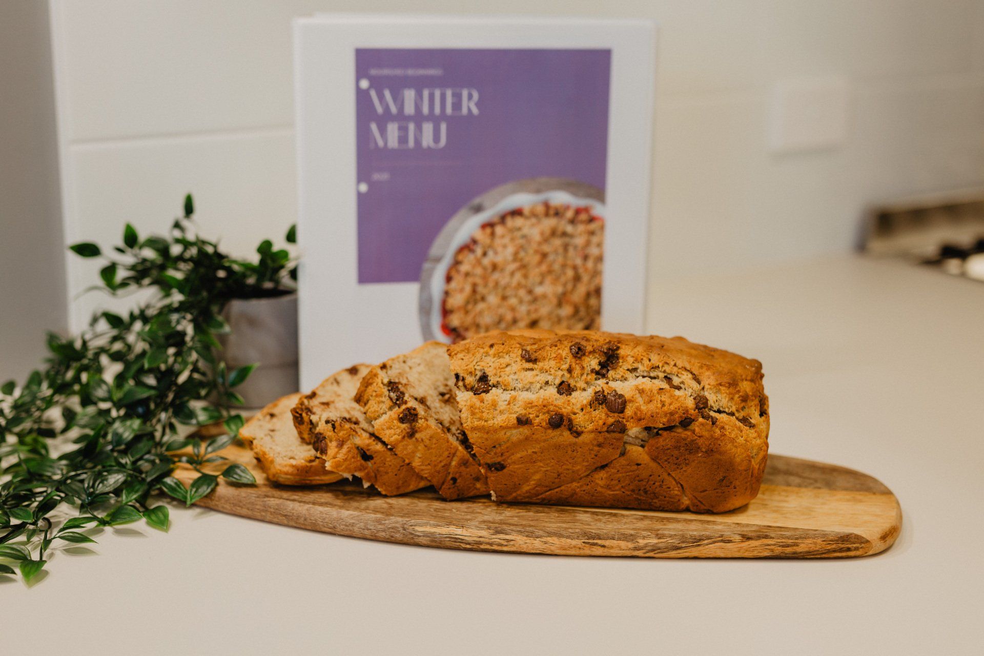 A freshly baked loaf of bread on a cutting board next to a book at Sagewood Canning Vale Campus Childcare Centre.