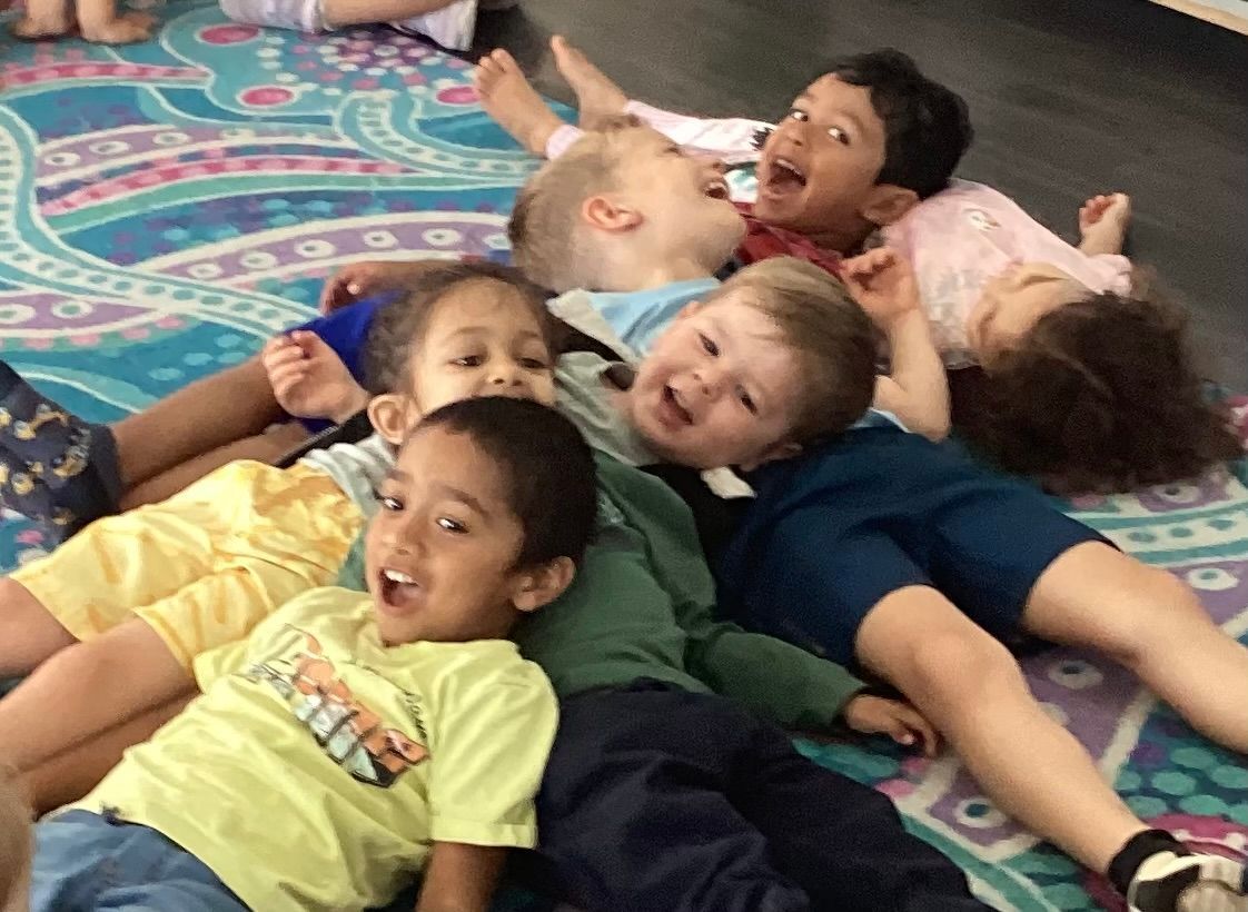 A group of children lying on the classroom floor at Sagewood Elma Campus - Childcare Centre, sharing laughter and joy.