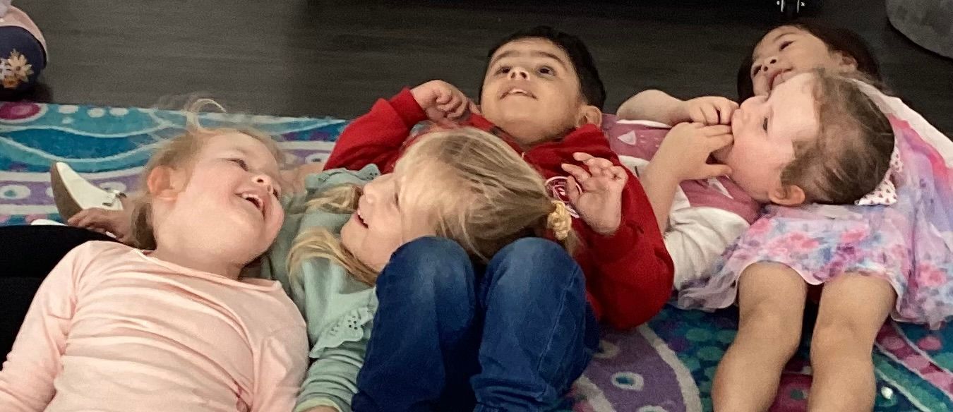 A group of children happily laying on the floor at Sagewood Elma Campus Childcare Centre, enjoying their playtime together.