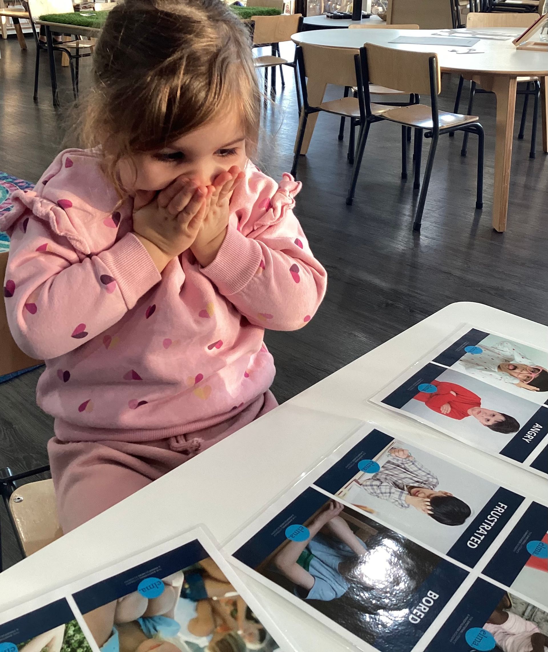 A little girl at a table surrounded by colorful pictures, enjoying her time at Sagewood Elma Campus - Childcare Centre.