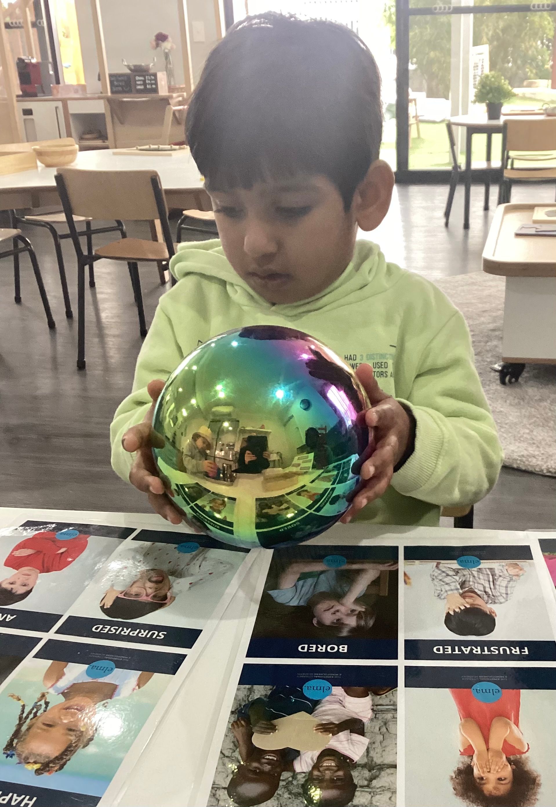 A happy young boy at Sagewood Elma Campus holds a bright, colorful ball, eager to play at the childcare center.