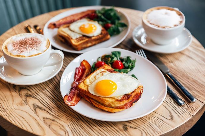 Tre piatti di cibo e due tazze di caffè su un tavolo di legno.