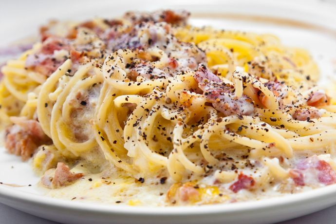 Un primo piano di un piatto di pasta con sugo e pancetta su un tavolo.