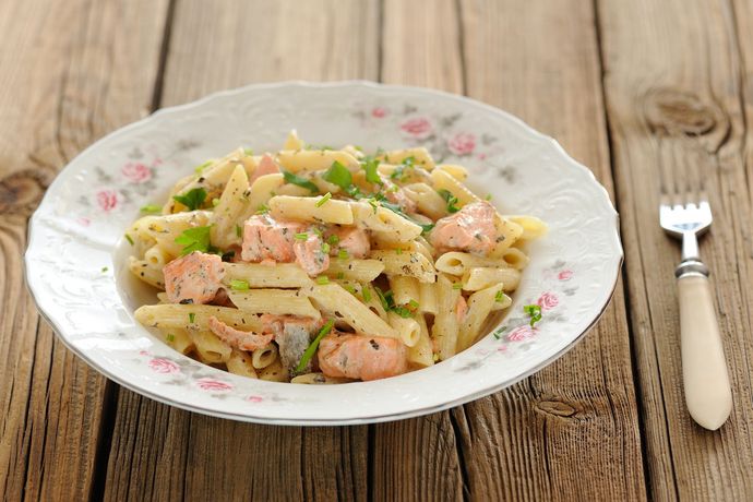 Un piatto di pasta al salmone e una forchetta su un tavolo di legno.