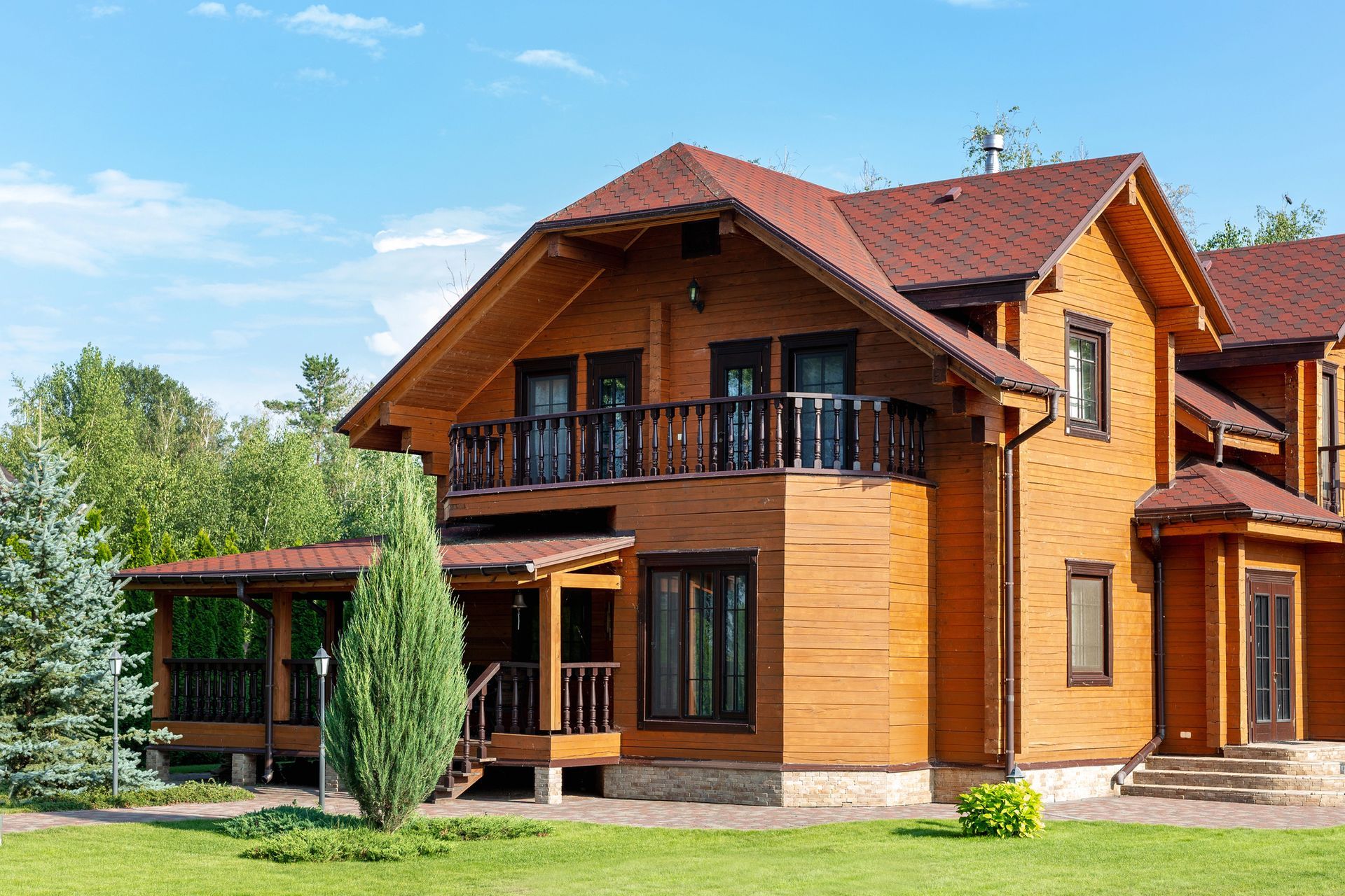 Moderna casa in legno a due piani con balcone, tetto rosso e prato verde sotto un cielo azzurro.