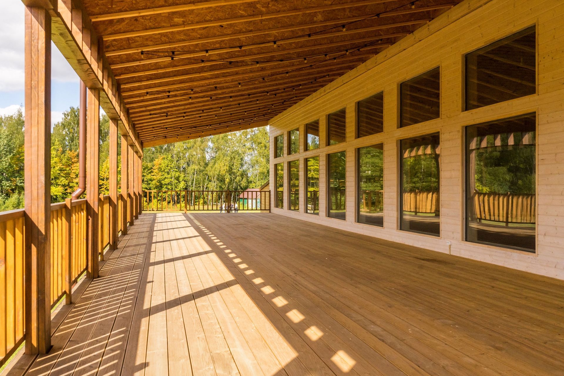 Veranda in legno con ringhiere e grandi finestre, illuminata da una calda luce solare che proietta lunghe ombre.