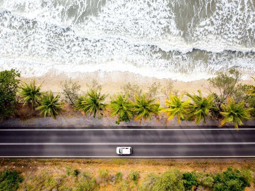 An Aerial View of a Car Driving Down a Road Next to the Ocean — Cairns Floors and More In Clifton Beach, QLD