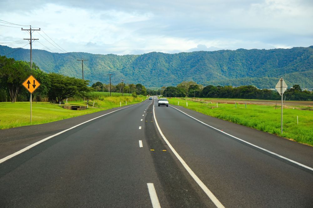 A Car is Driving Down a Highway With Mountains in the Background — Cairns Floors and More In Edmonton, QLD