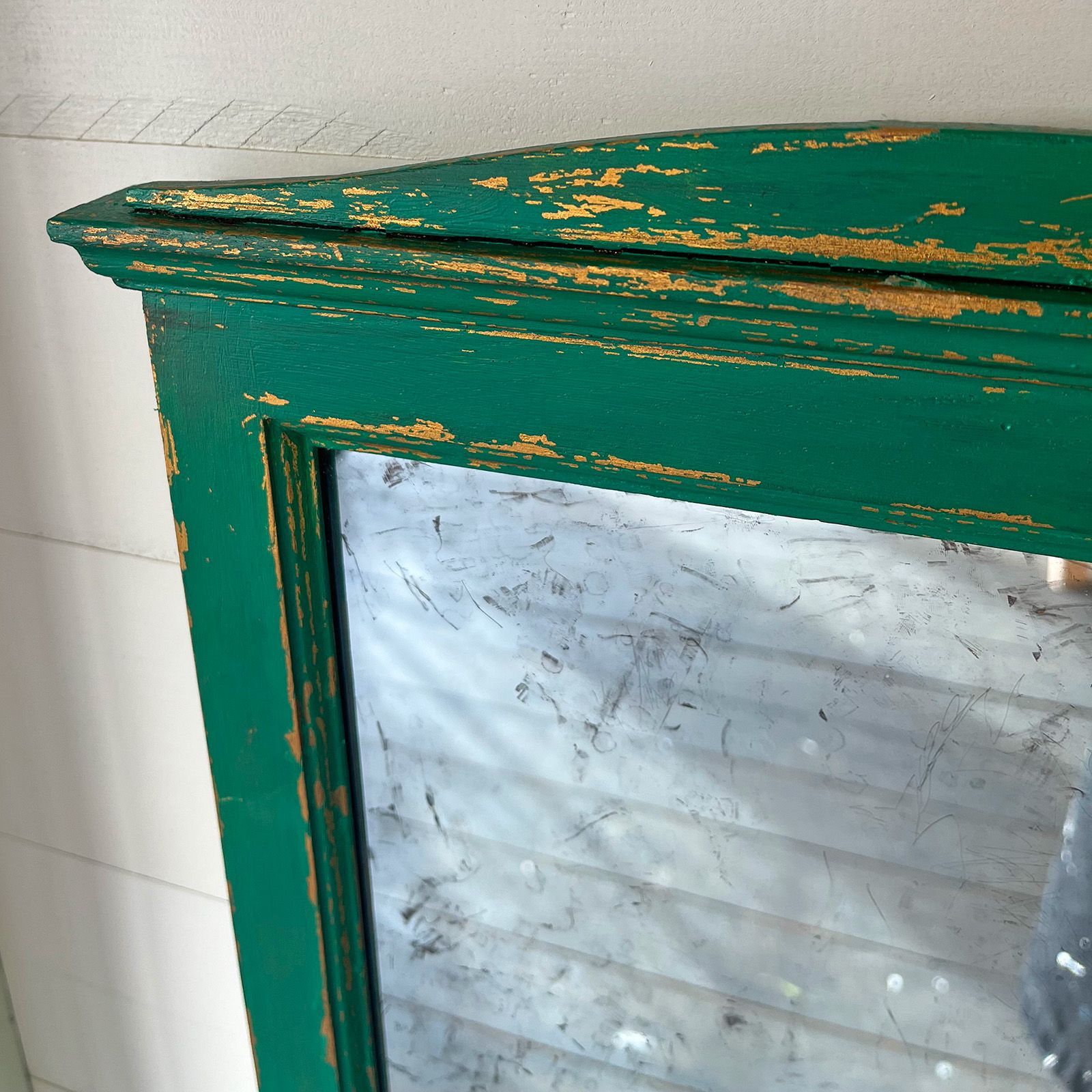 Detail of a upcycled mirror frame with a gold base paint and a distressed emerald top coat.