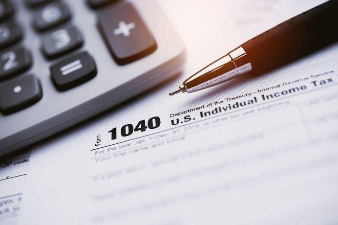Una penna è appoggiata su un modulo fiscale 1040 accanto a una calcolatrice.
