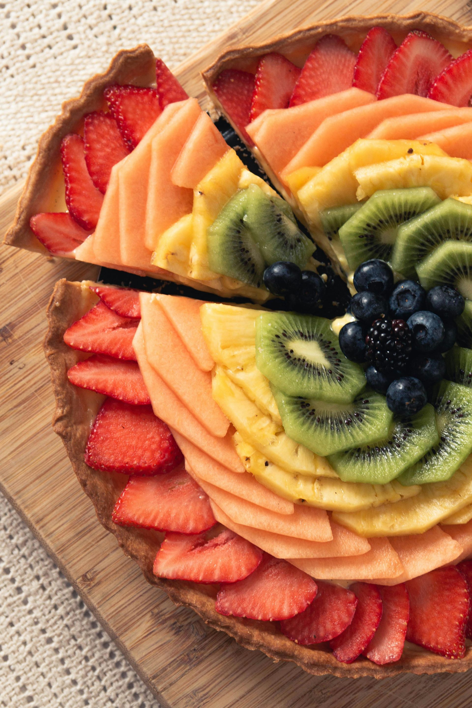 Tarta de frutas con fresas, melón, piña, kiwi y bayas dispuestas en capas de colores.