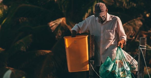 An elderly man carrying trash bags